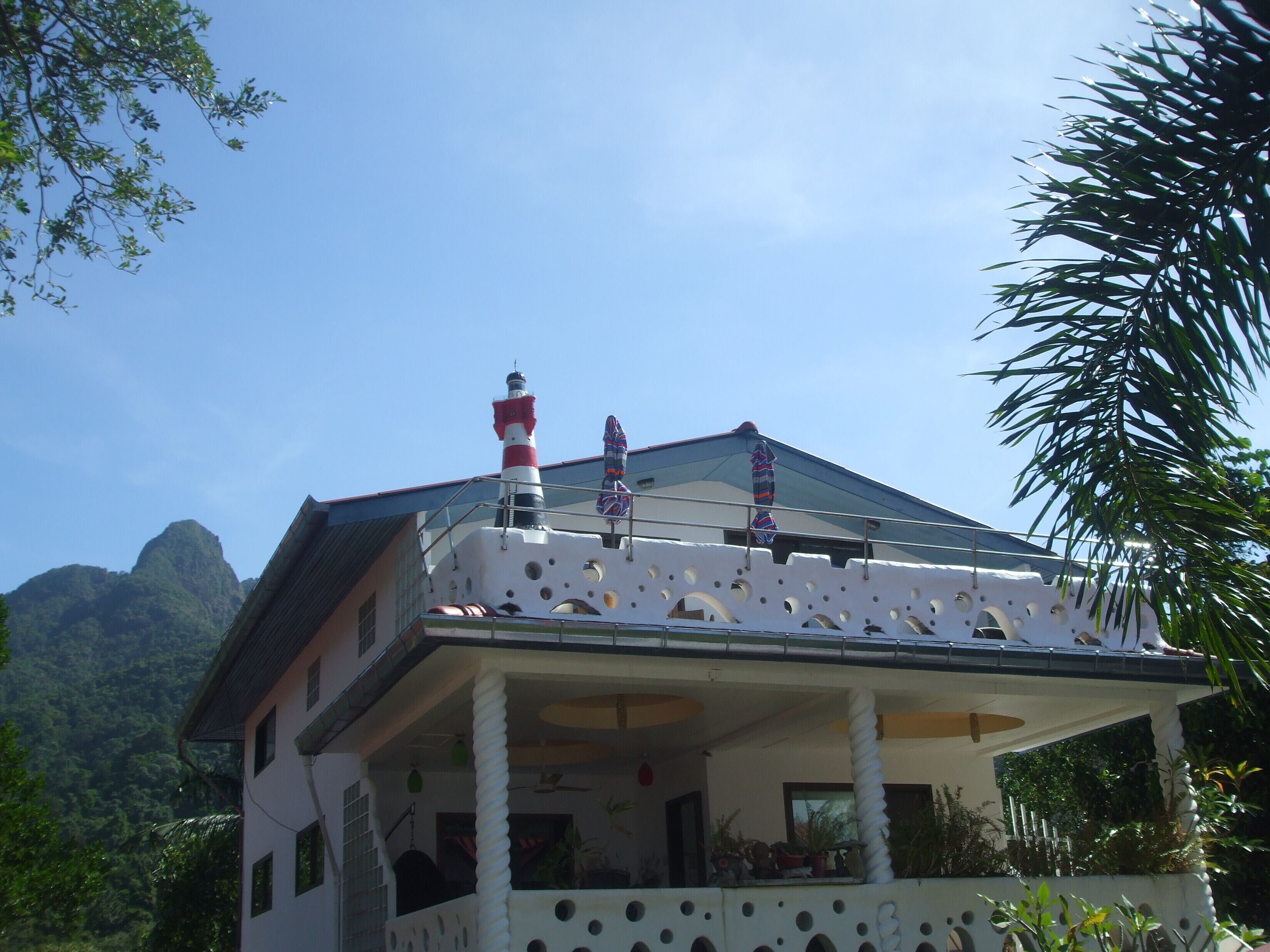 Una casa con balcón, un modelo de faro y una montaña al fondo.