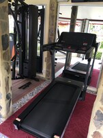 Un gimnasio con cinta de correr, máquinas de pesas y piso cubierto de alfombra roja.