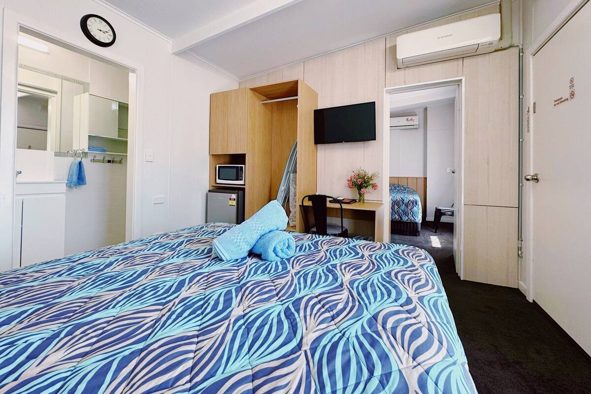 A hotel room with a bed, a TV, a microwave, and a small desk with a chair.
