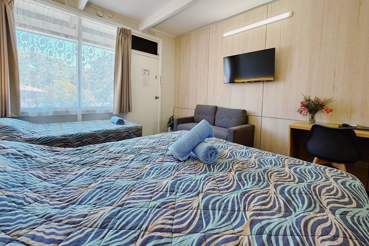 A hotel room with two beds, a sofa, a desk, and a TV.