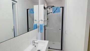 Un baño estrecho con un lavamanos blanco, un espejo y un box de ducha de vidrio.