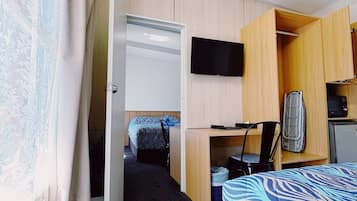 Una habitación funcional con cama, escritorio, televisor y armario.