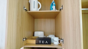 A kitchen with wooden cabinets, a coffee maker, an iron, a tea box, and a microwave. - Seymour Motel (Seymour)