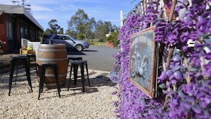 A rustic building with a gravel patio, a vintage motorcycle, and purple flowers. - Seymour Motel (Seymour)