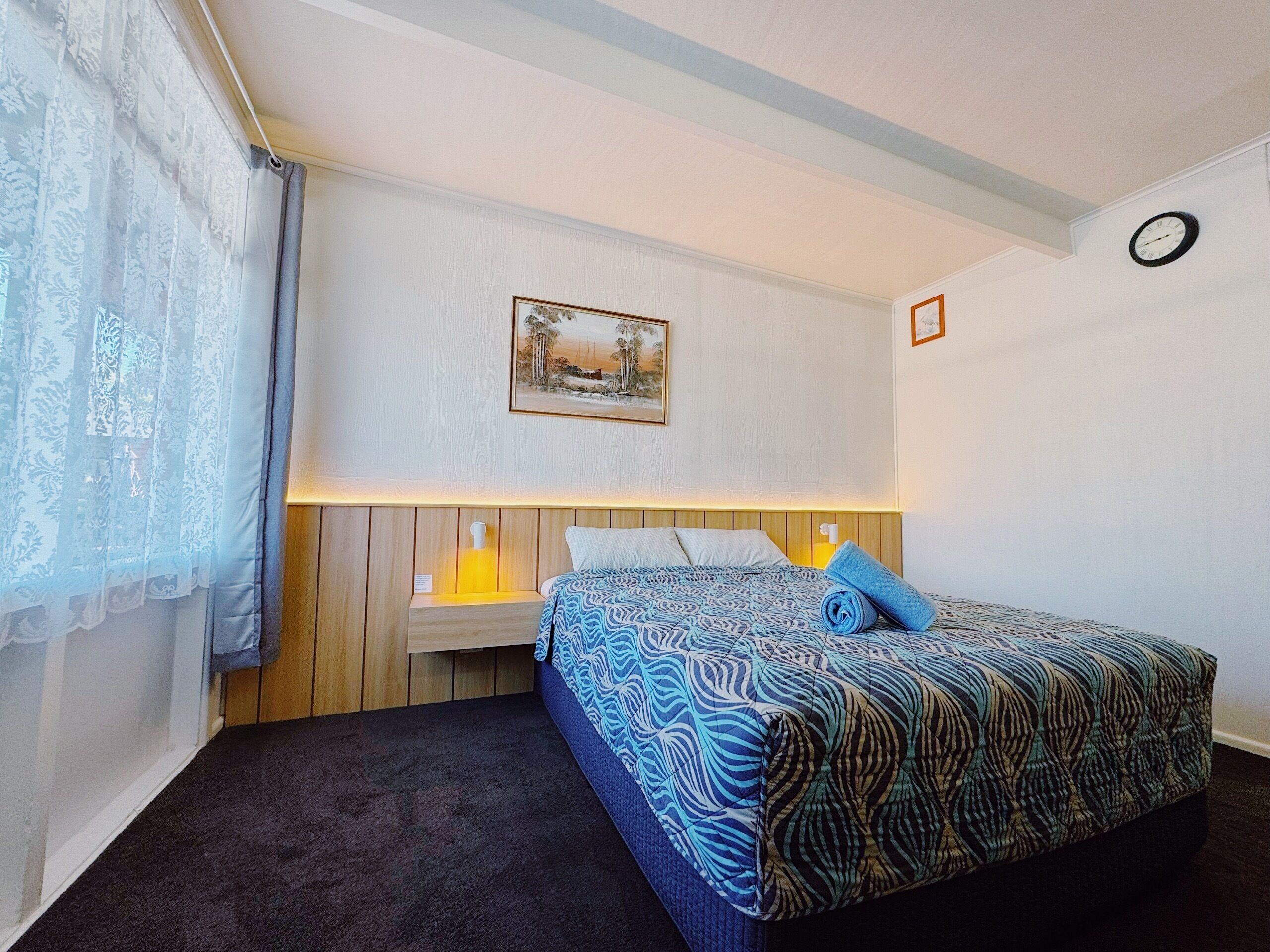 Ein Schlafzimmer mit einem Bett, einem Nachttisch, einer Lampe, einem Gemälde und einer Wanduhr.