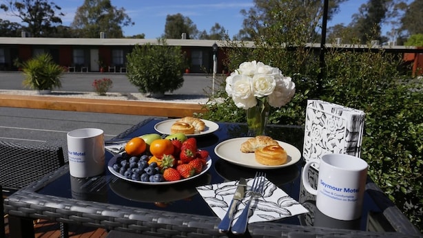 A table with breakfast items, a vase of white flowers, and a menu on a sunny outdoor patio. - Seymour Motel (Seymour)