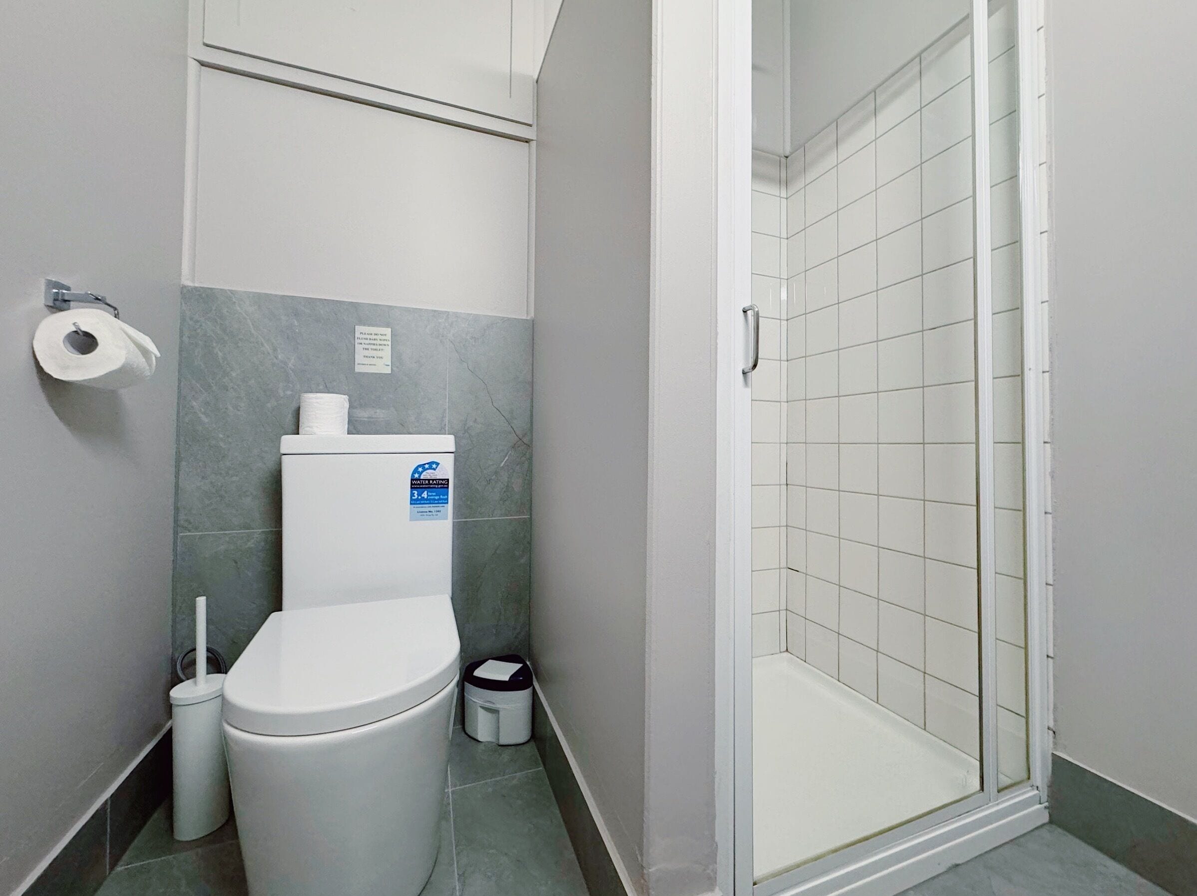 A bathroom with a toilet, a shower, and a trash bin.