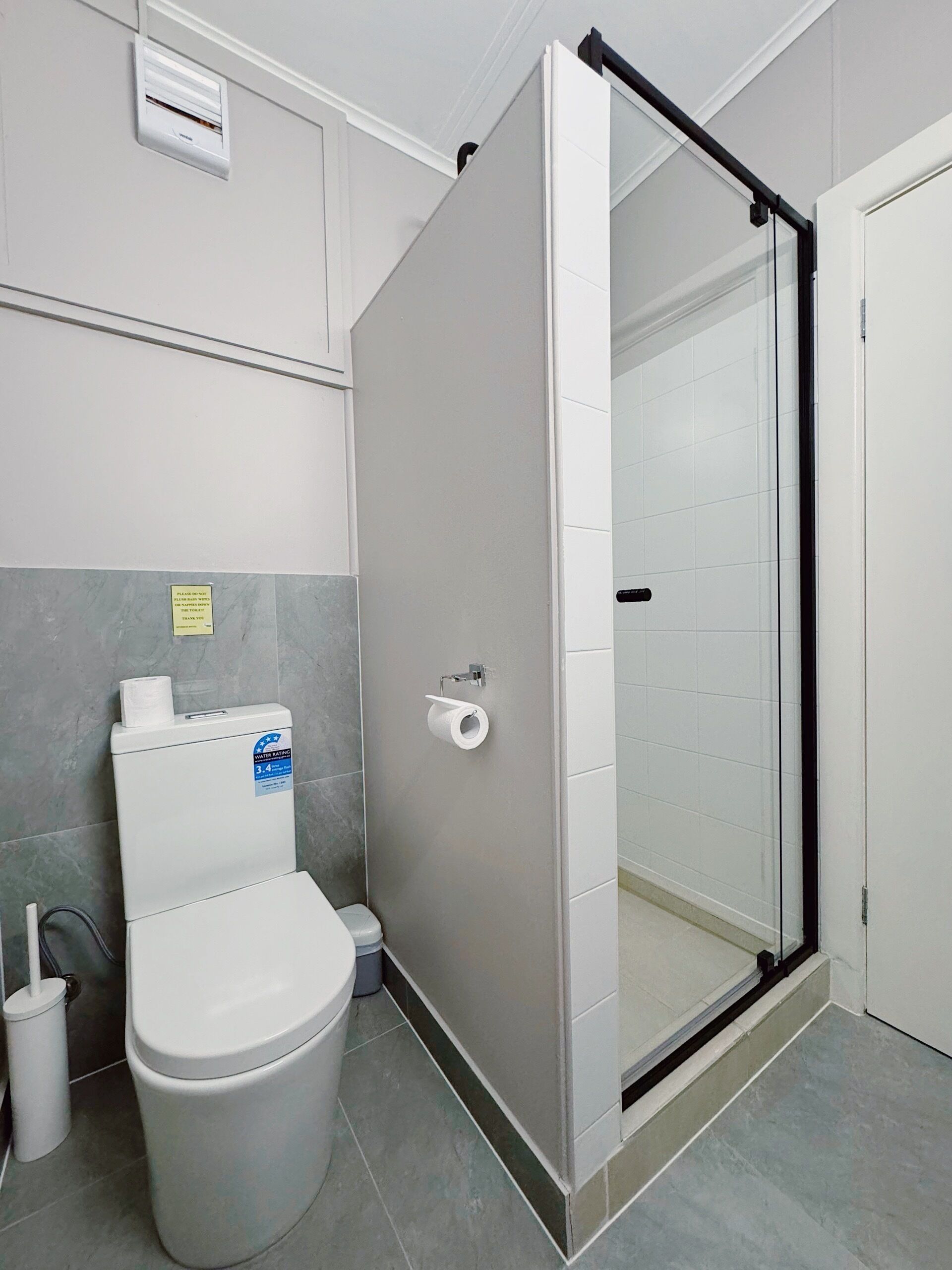 Une salle de bain équipée de toilettes, d’un distributeur d’essuie-tout, d’une douche en verre et d’un climatiseur fixé au mur.