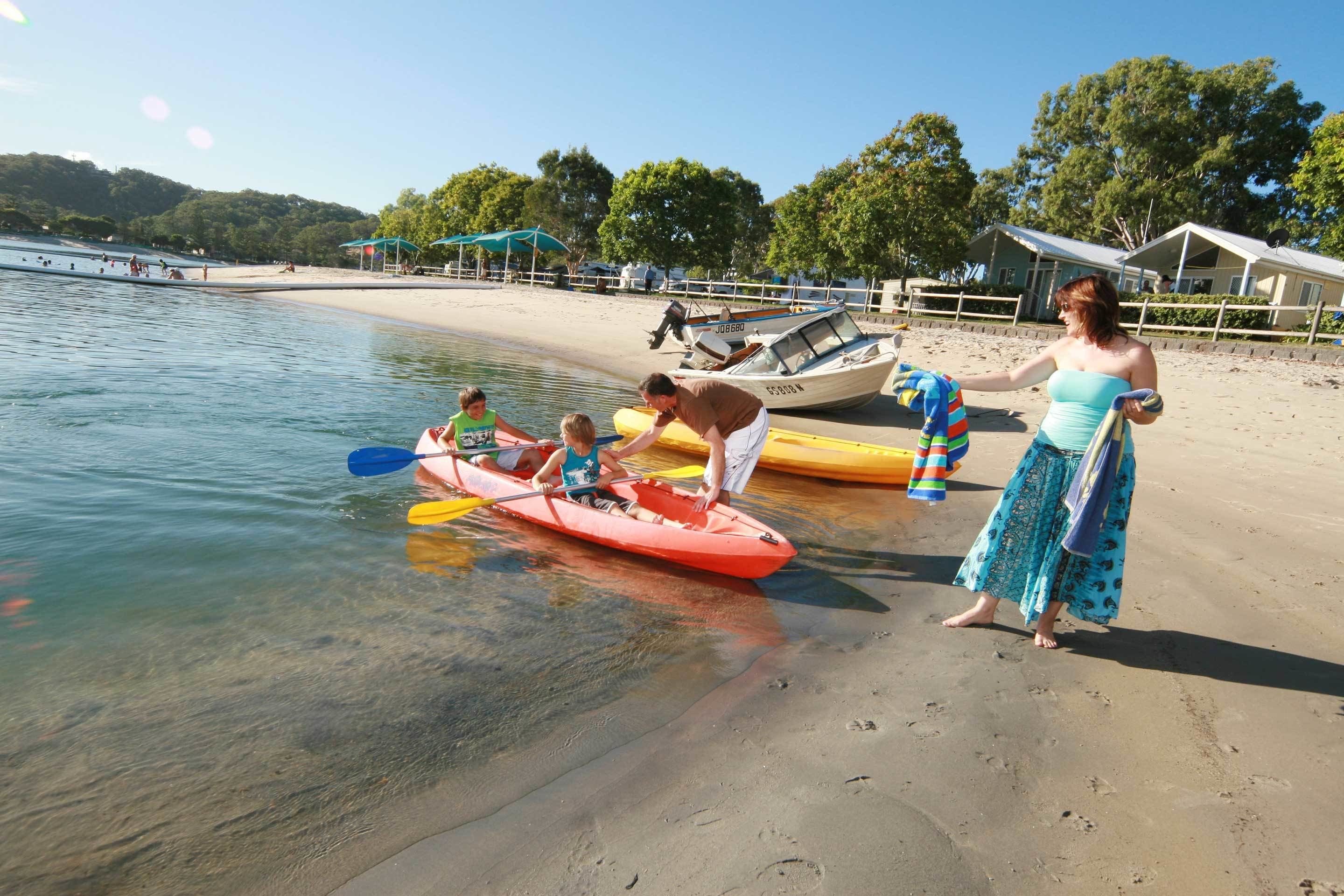 A beach with kayaks, a boat, and a woman standing on the sand.