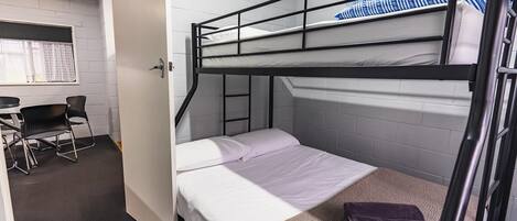 Habitación con literas, escritorio y silla, paredes blancas y una ventana.