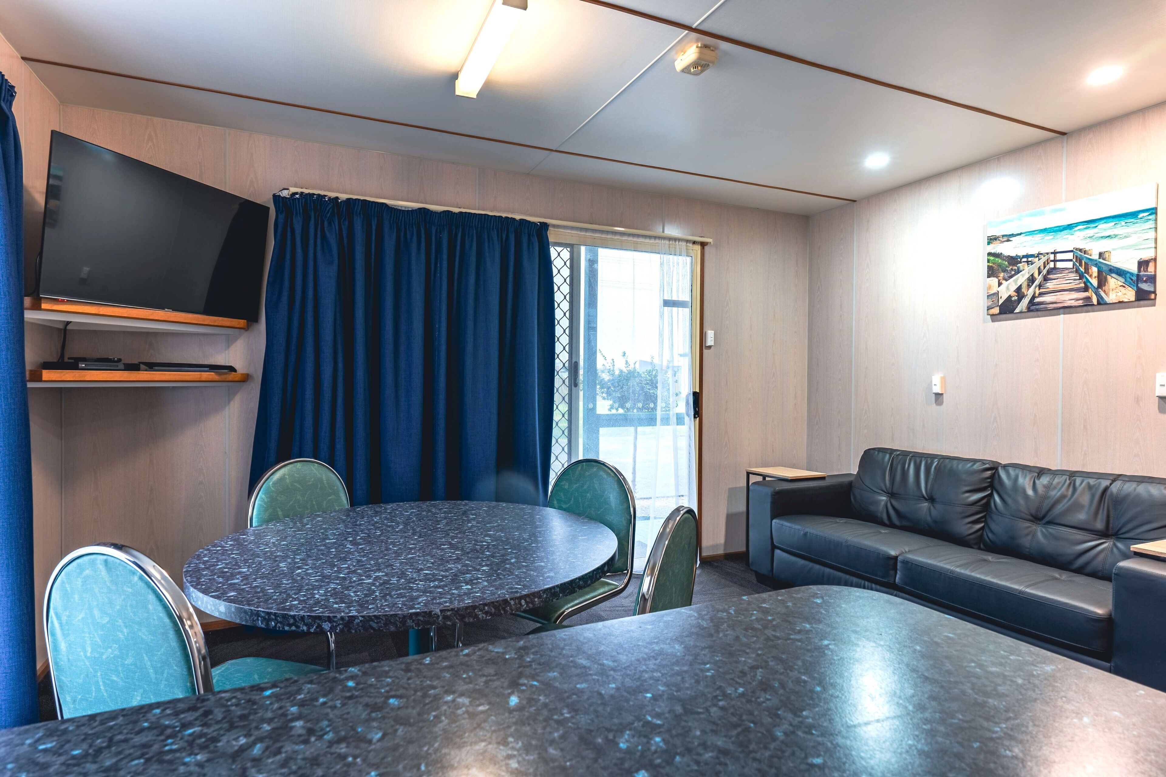 A modern room with a round table, chairs, a sofa, a flat-screen TV, and a window with curtains.