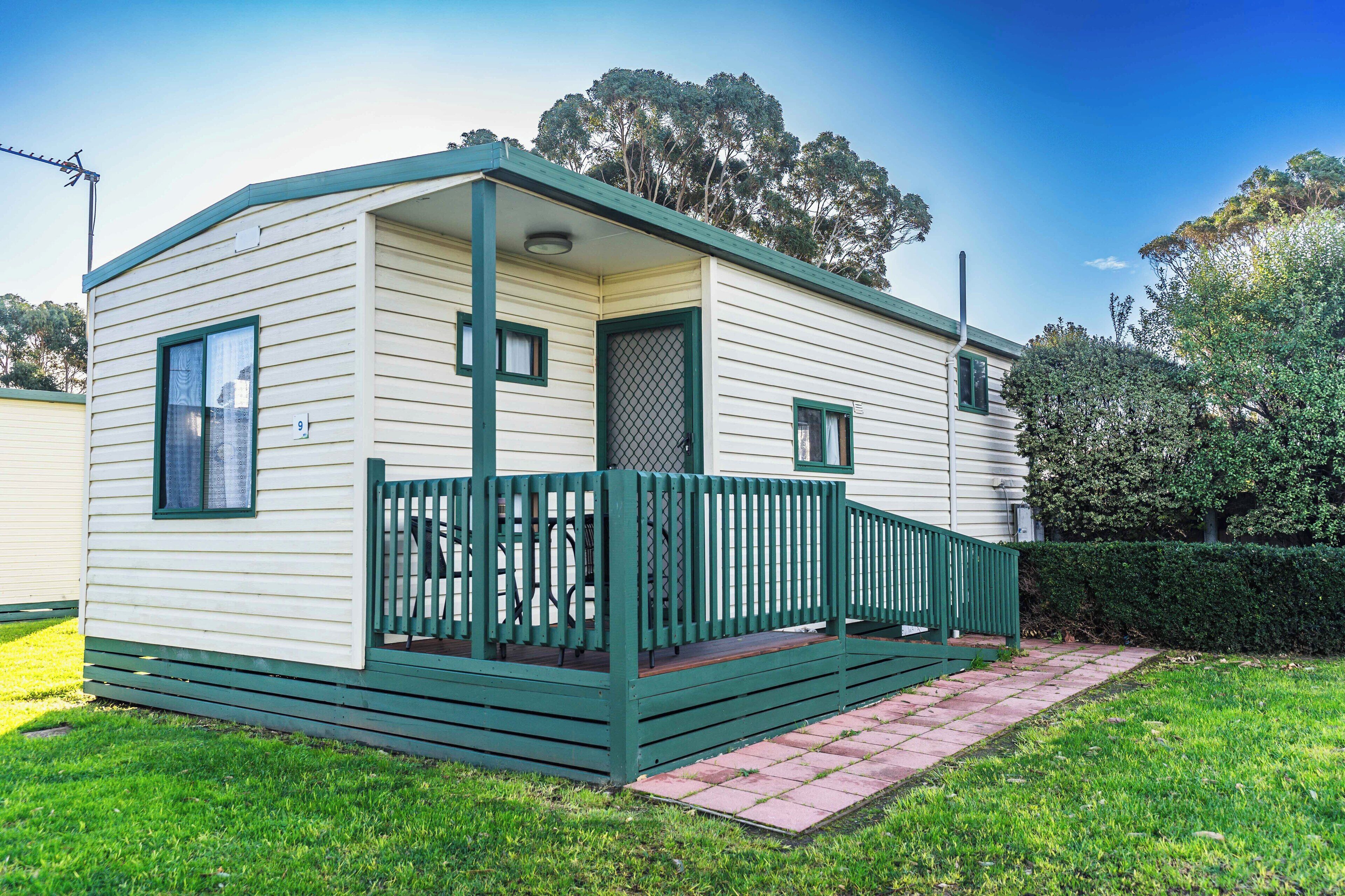 A single-story mobile home with a green porch and a small window.