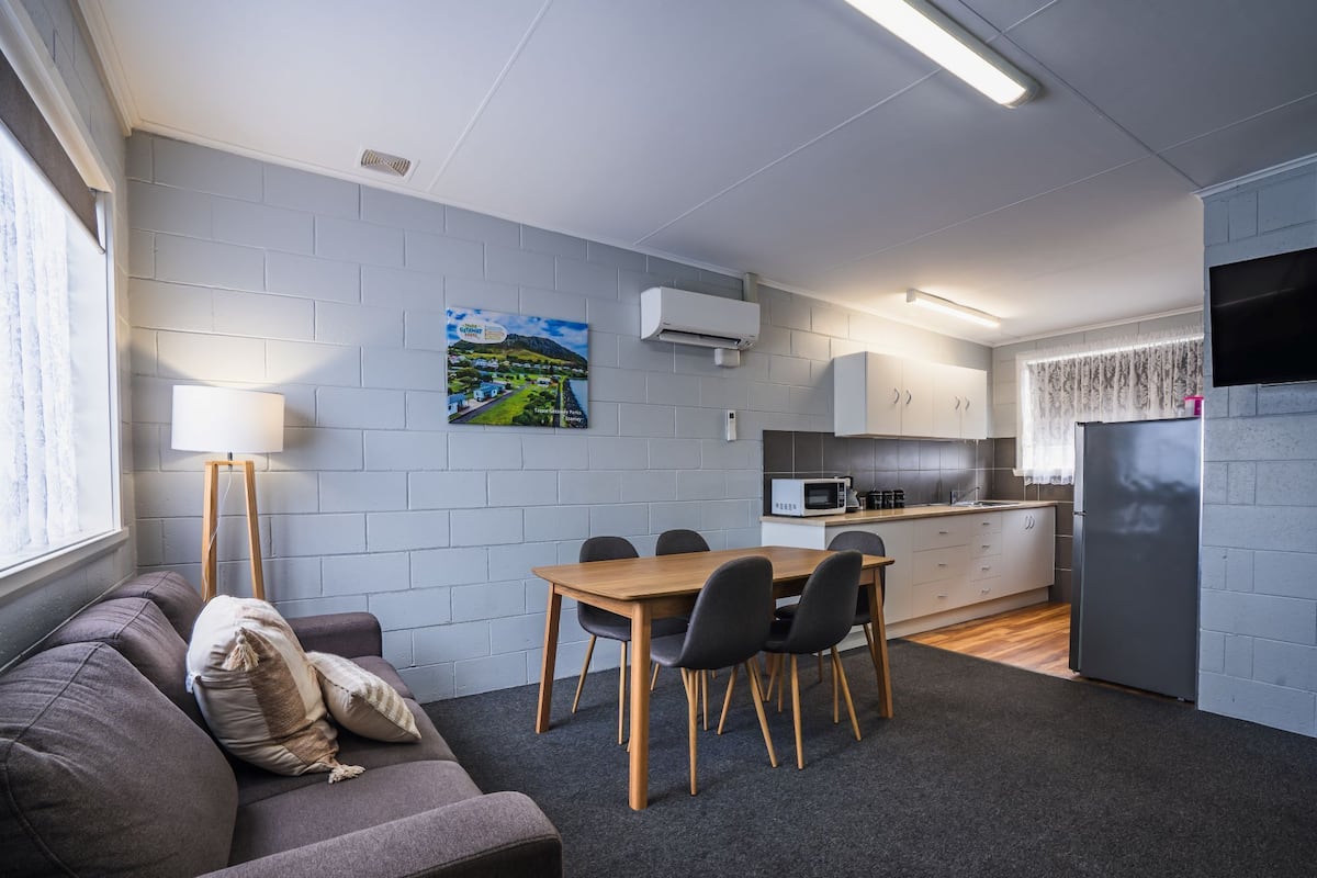 Un espacio habitable compacto con comedor, kitchenette y un sofá con cojines.