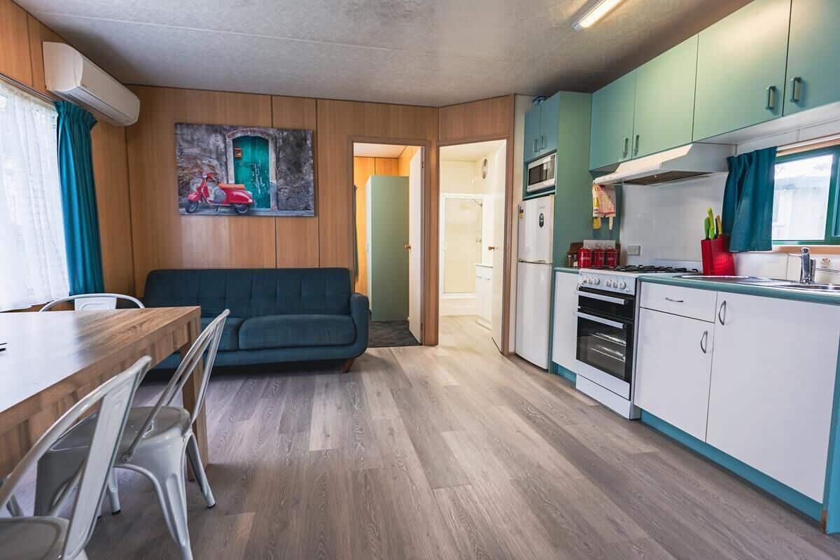 Un espacio habitable compacto con comedor, sofá, kitchenette y una puerta que da a otra habitación.