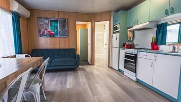 A compact living space with a dining area, a sofa, a kitchenette, and a door leading to another room.