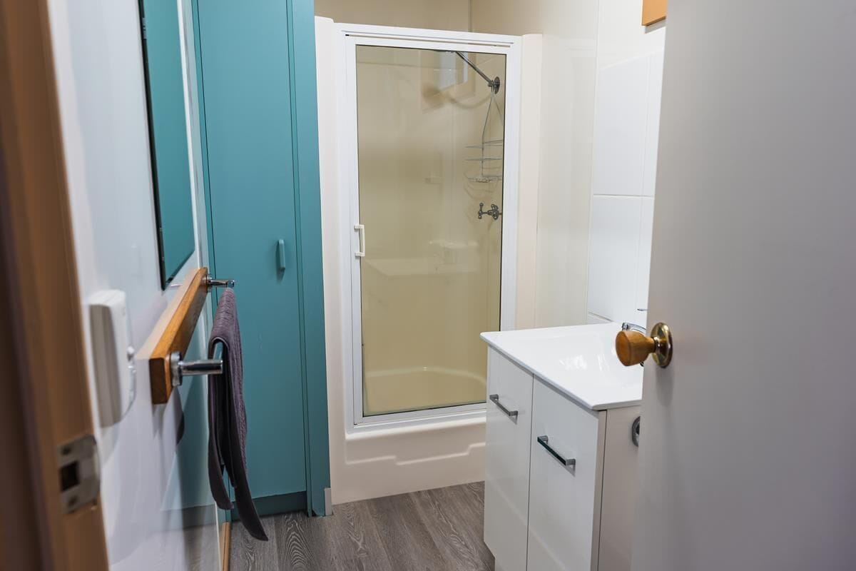 A bathroom with a shower, a white sink, and a door with a towel hanging on a rack.