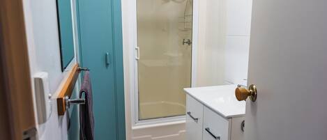A bathroom with a shower, a white sink, and a door with a towel hanging on a rack.