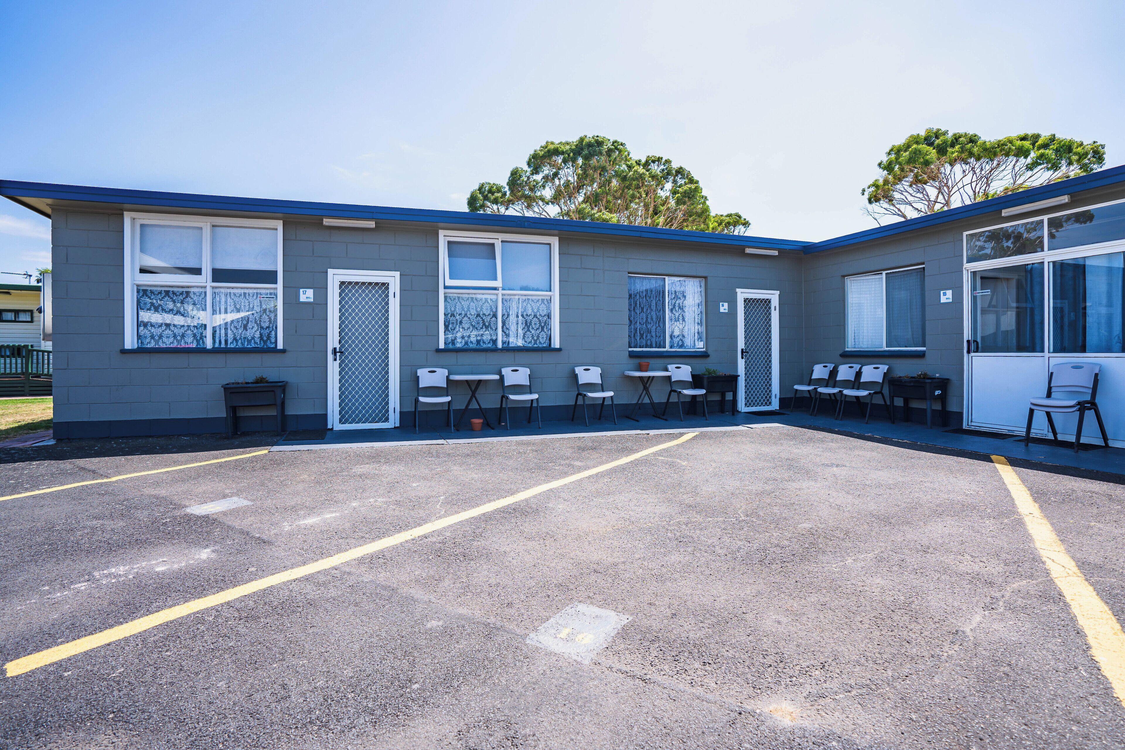 A motel with a parking lot, outdoor seating area, and a fenced yard.