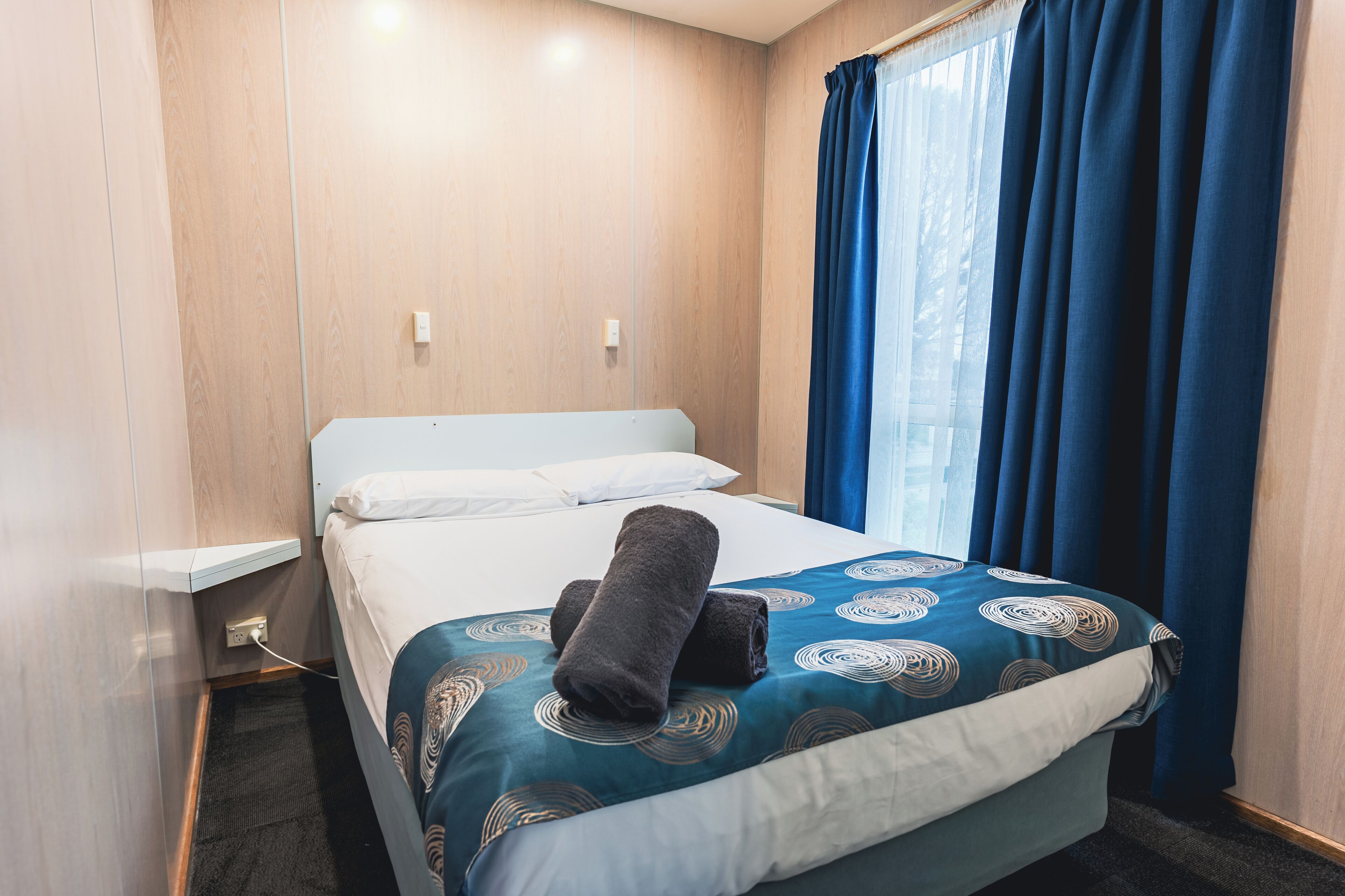 A hotel room with a bed, a nightstand, and a window with curtains.
