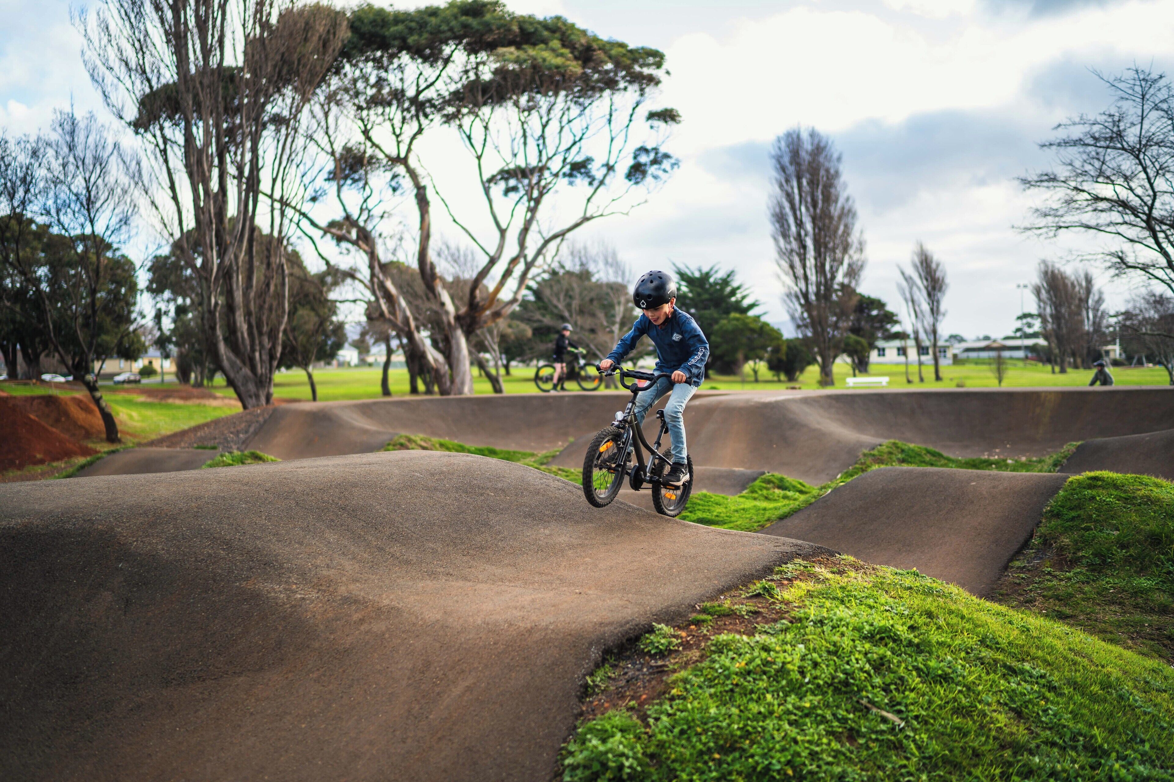 A person riding a bicycle on a concrete track surrounded by grass and trees.