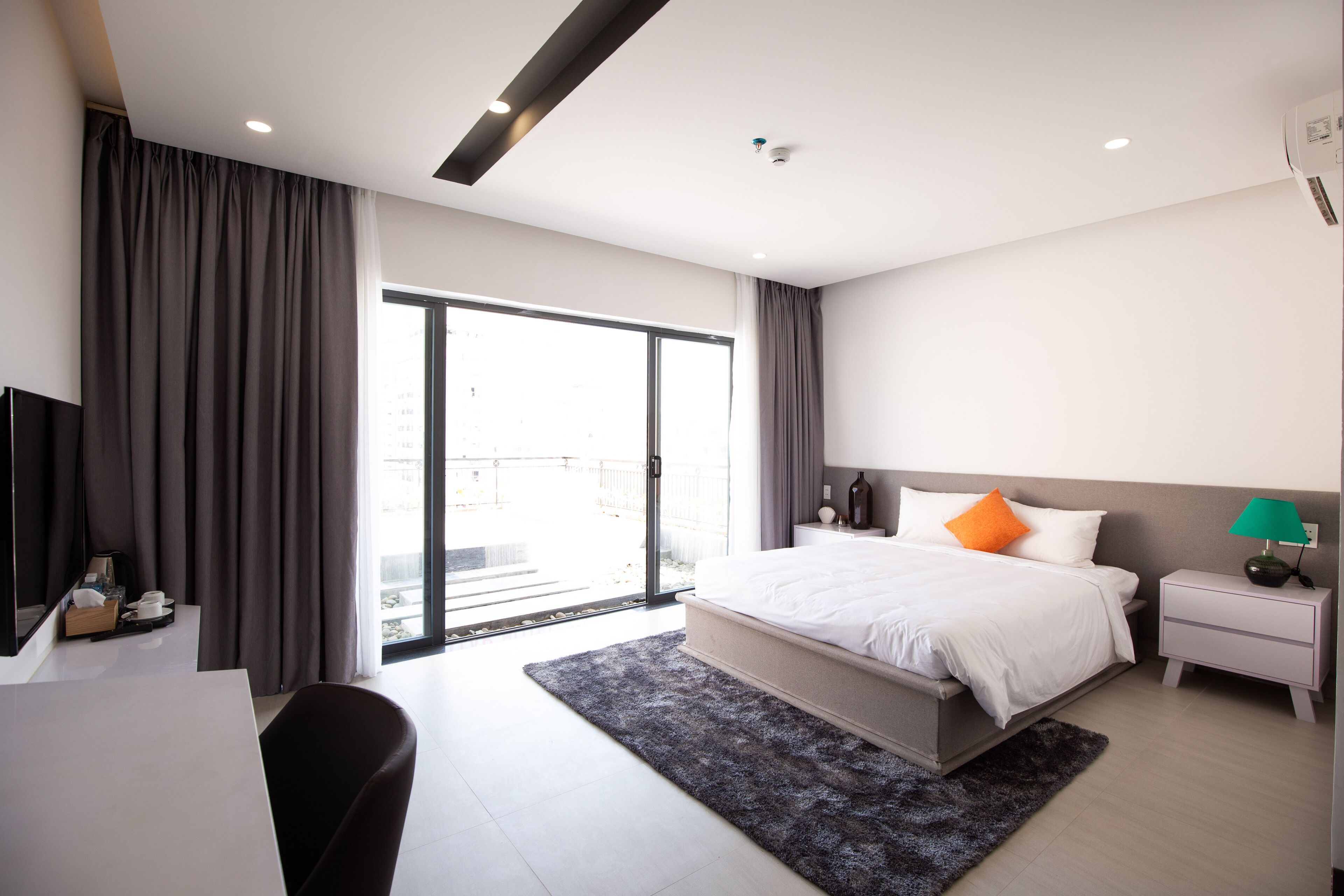 A modern hotel room with a large bed, a desk, and a view through a sliding glass door.