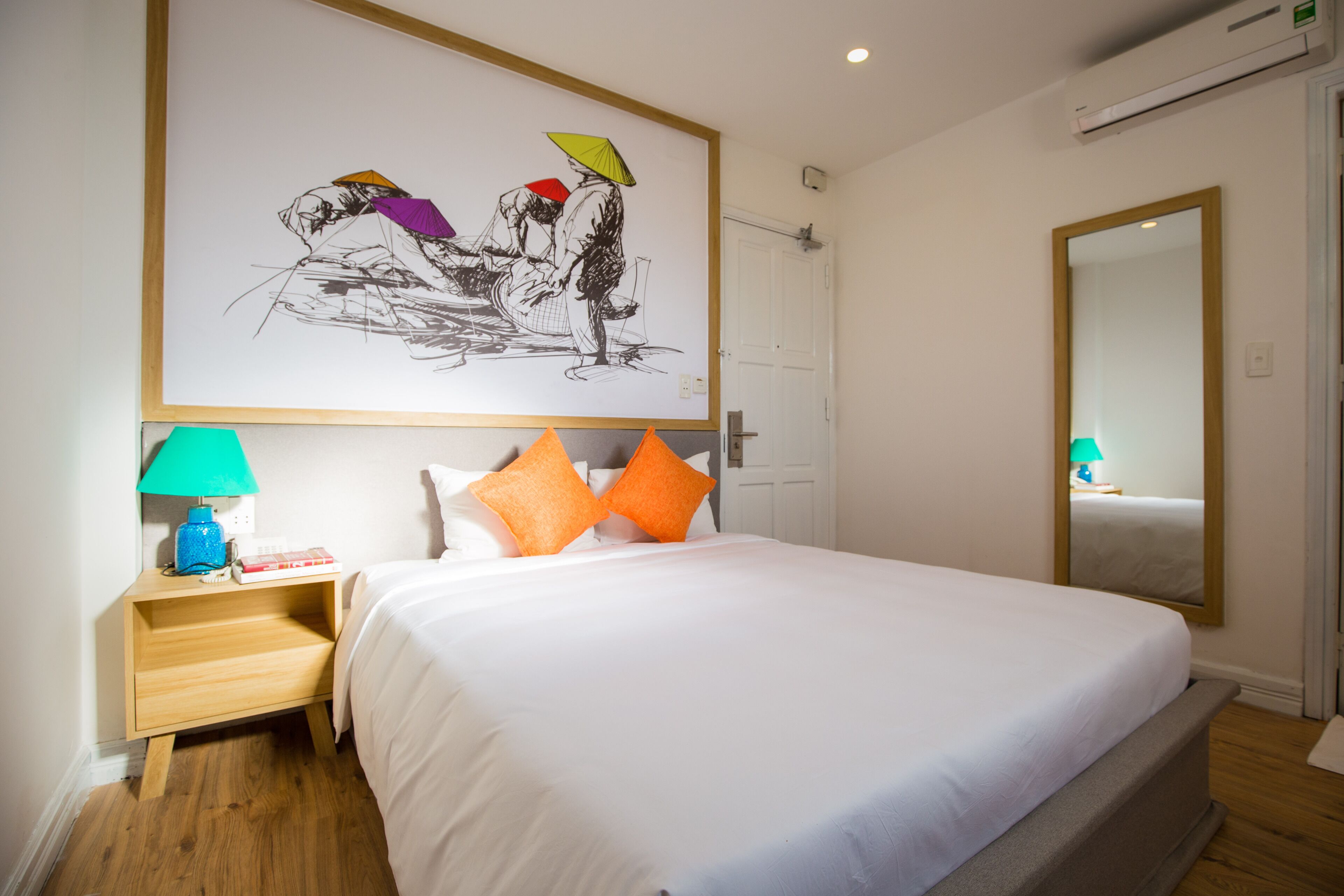 A hotel room with a large bed, a nightstand with a lamp, a wall-mounted artwork, and a mirror.