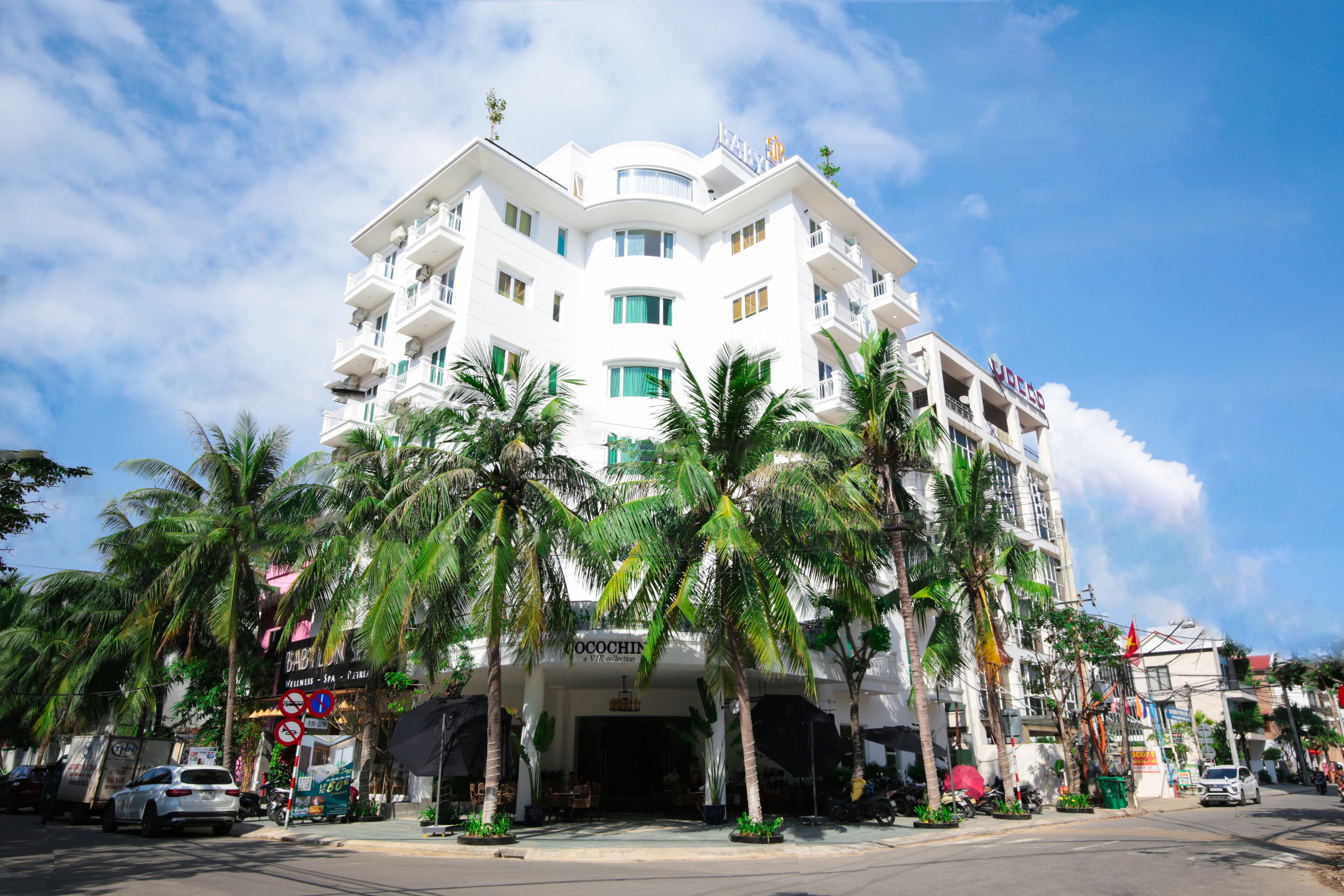 A multi-story hotel with balconies, palm trees, and a clear sky.