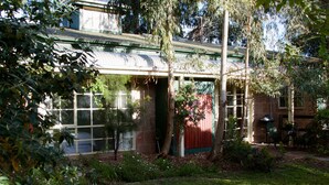 A house with a covered porch, a red door, and a garden with various plants and flowers. - Holly Lane Mews (Steels Creek)