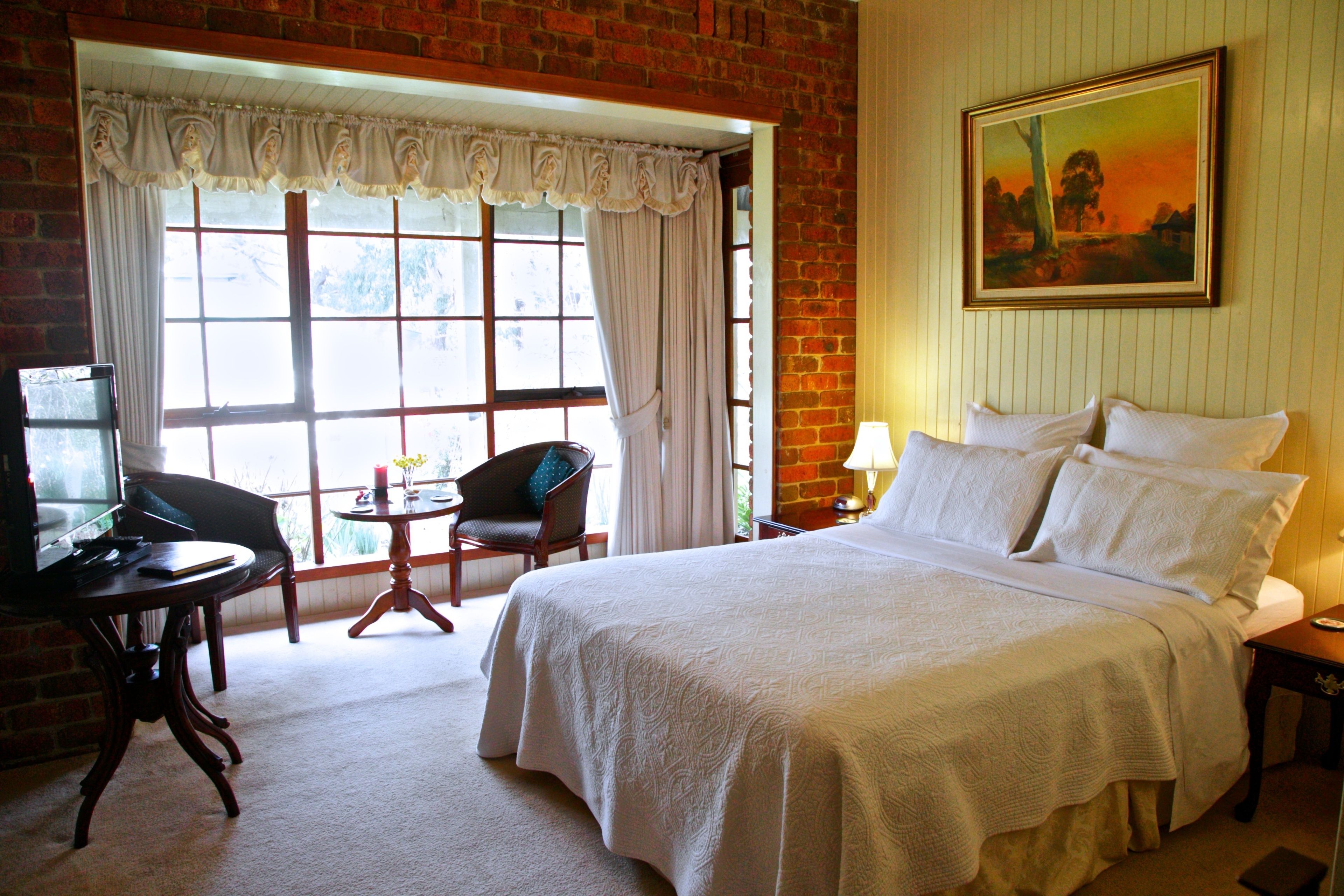 Een hotelkamer met een groot bed, een televisie, een stoel, een tafeltje en een raam met gordijnen.