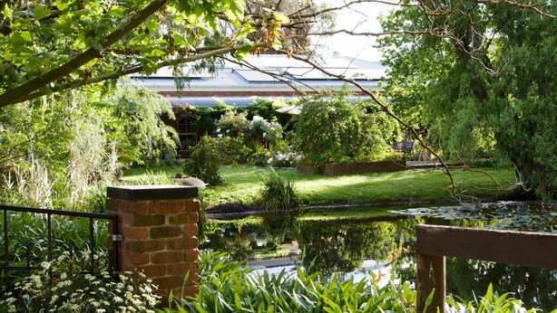 A garden with a pond, a brick wall, and a bench. - Holly Lane Mews (Steels Creek)