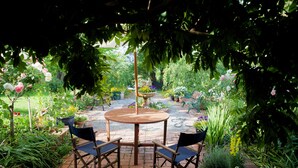 A garden patio with a round wooden table and four chairs, surrounded by various plants and flowers. - Holly Lane Mews (Steels Creek)
