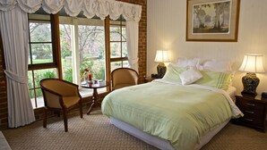 A bedroom with a large bed, two bedside tables with lamps, a chair, and a window with curtains. - Holly Lane Mews (Steels Creek)