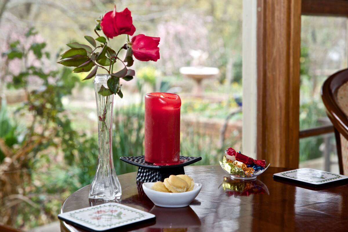 A table with a candle, a vase with roses, a bowl of macarons, and a plate with a dessert.