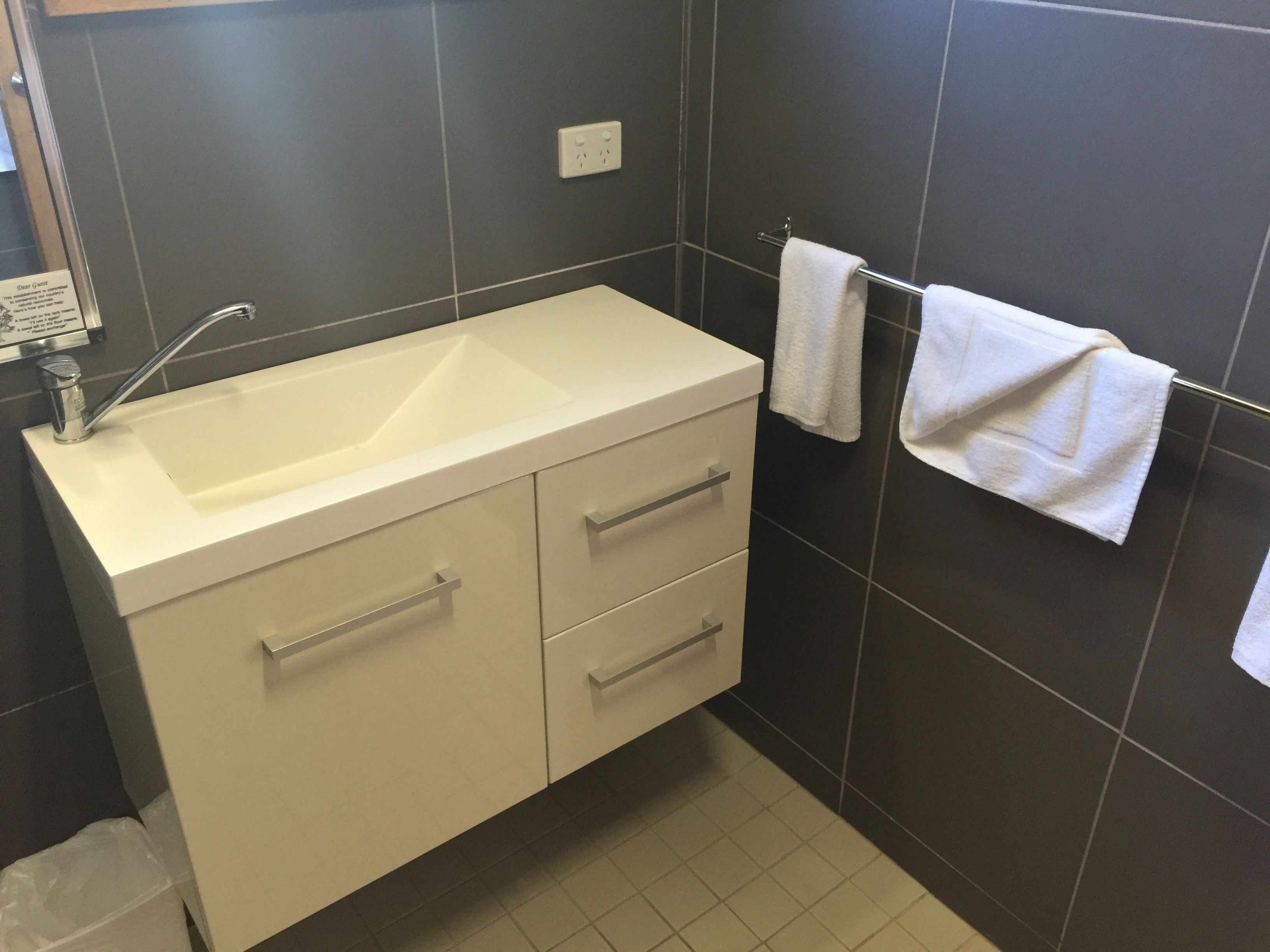A bathroom with a white sink, two drawers, a towel rack with two towels, and a trash bin.