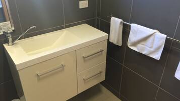 A bathroom with a white sink, two drawers, a towel rack with two towels, and a trash bin.