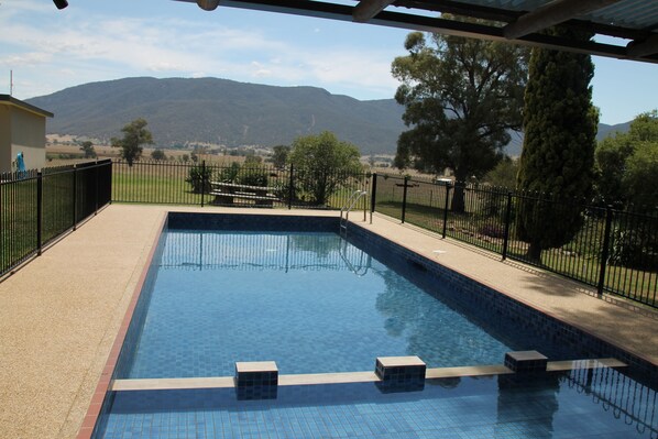 A rectangular swimming pool with a tiled edge, surrounded by a black metal fence, and a view of distant hills and trees.