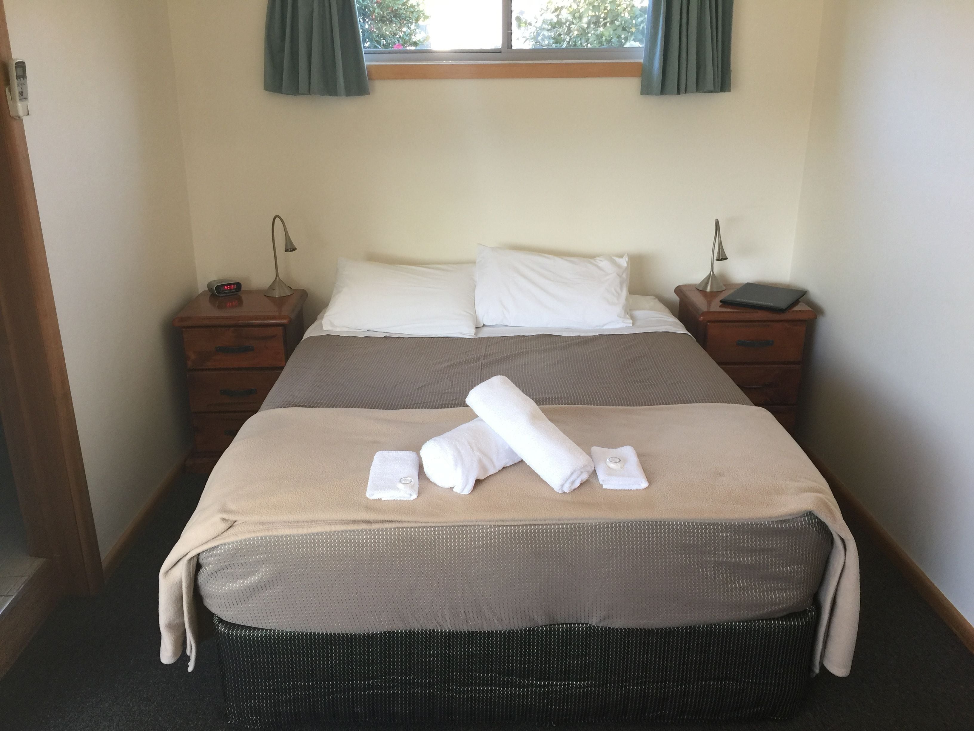 A neatly made bed with white linens, two bedside tables with lamps, and a window with curtains.