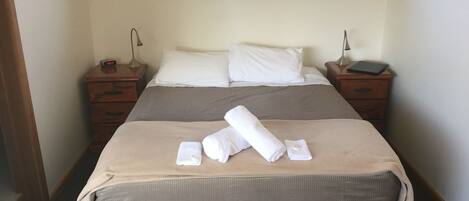 A neatly made bed with white linens, two bedside tables with lamps, and a window with curtains.