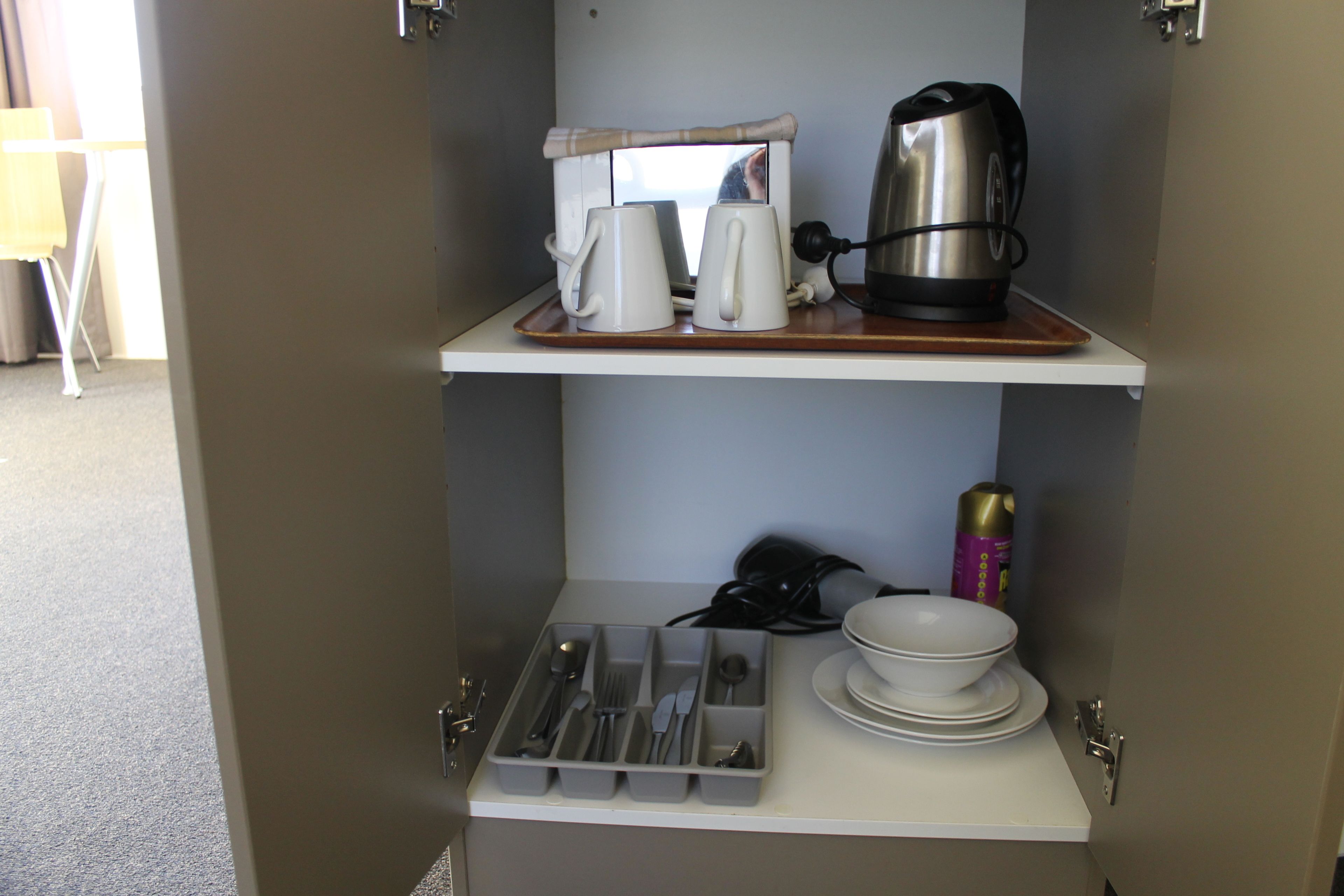 Una kitchenette equipada con cafetera, tazas, una lata de café y un juego de utensilios.