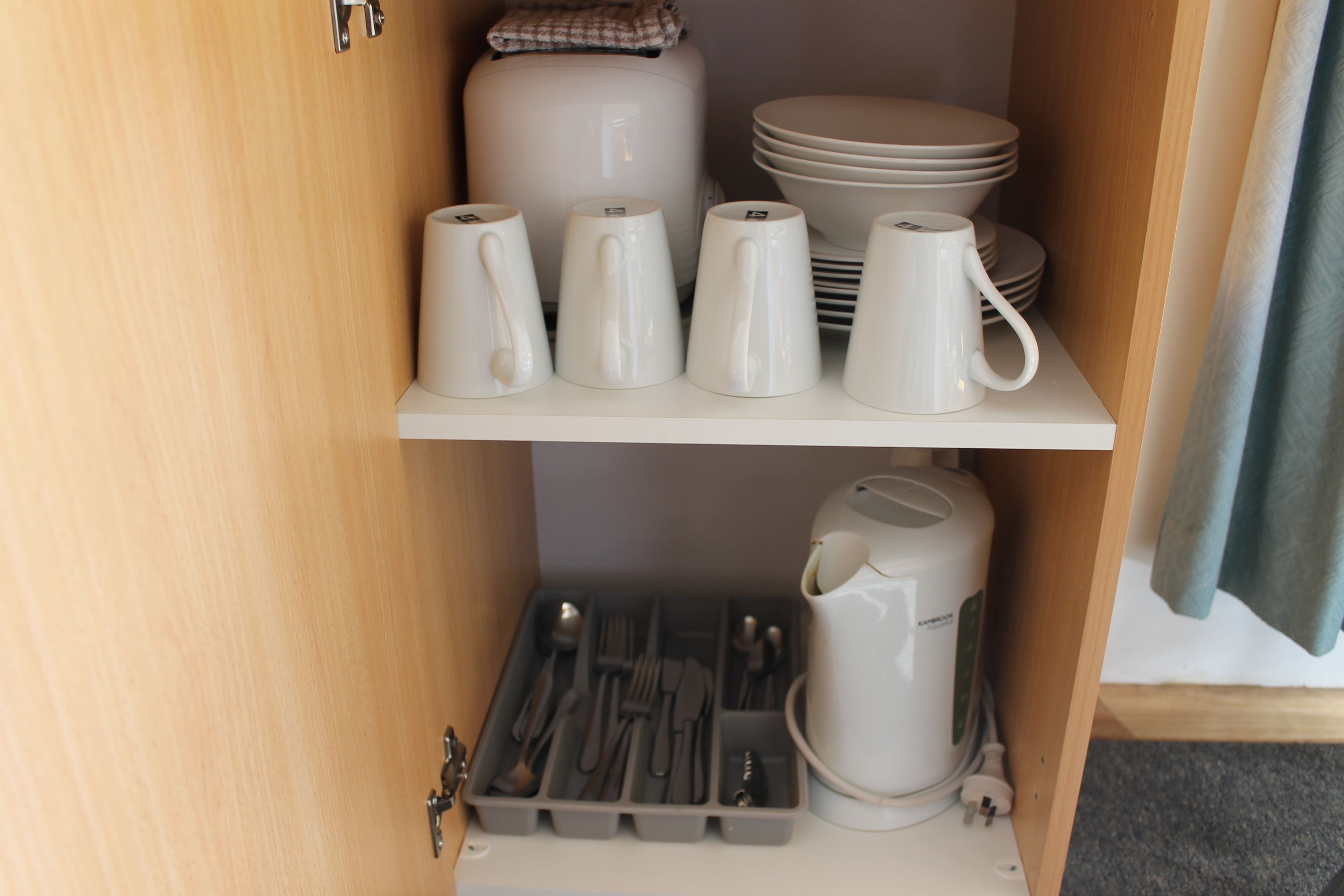 Een keukenkastje met witte mokken, borden en een waterkoker.
