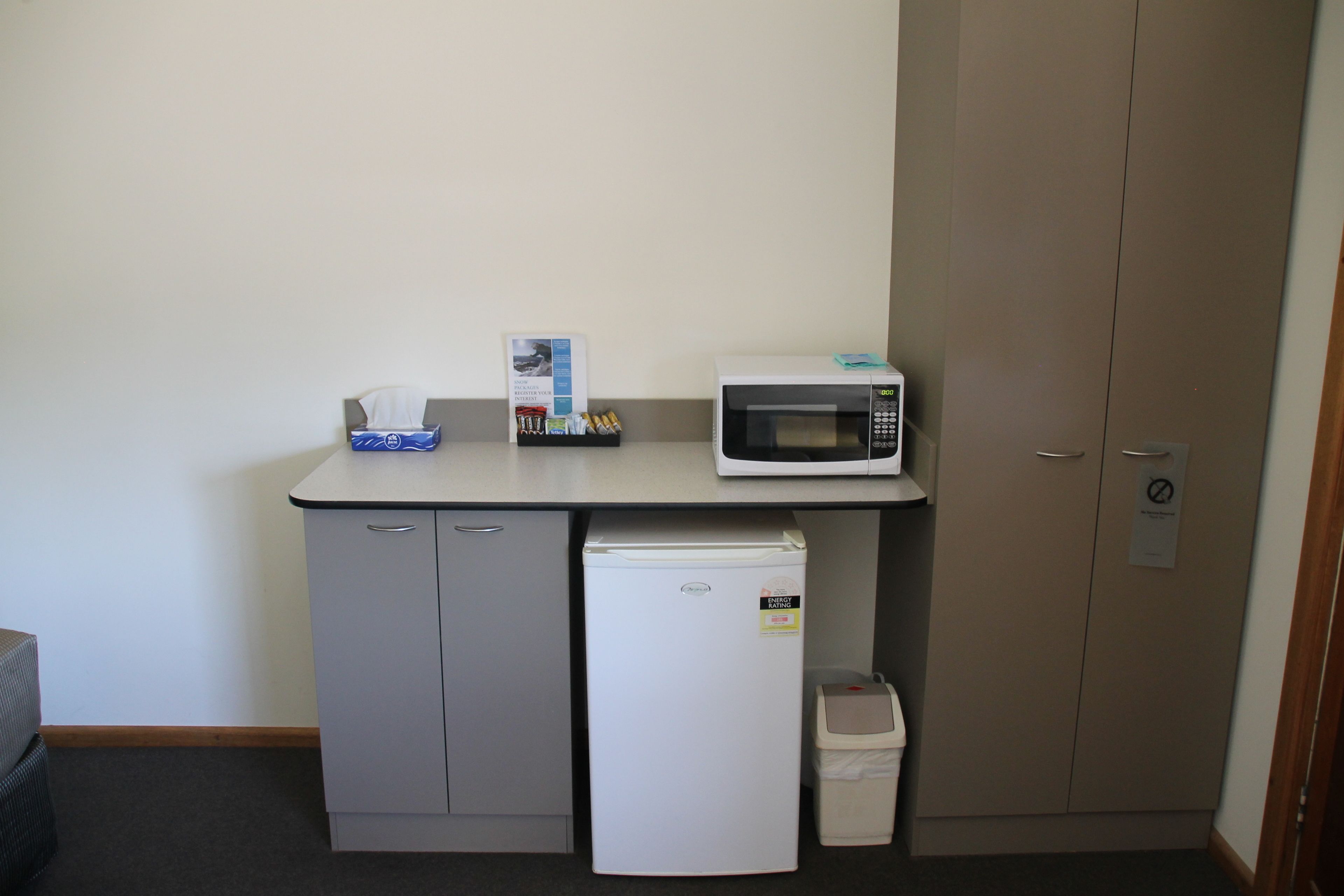 A kitchenette with a microwave, refrigerator, and a small trash bin.