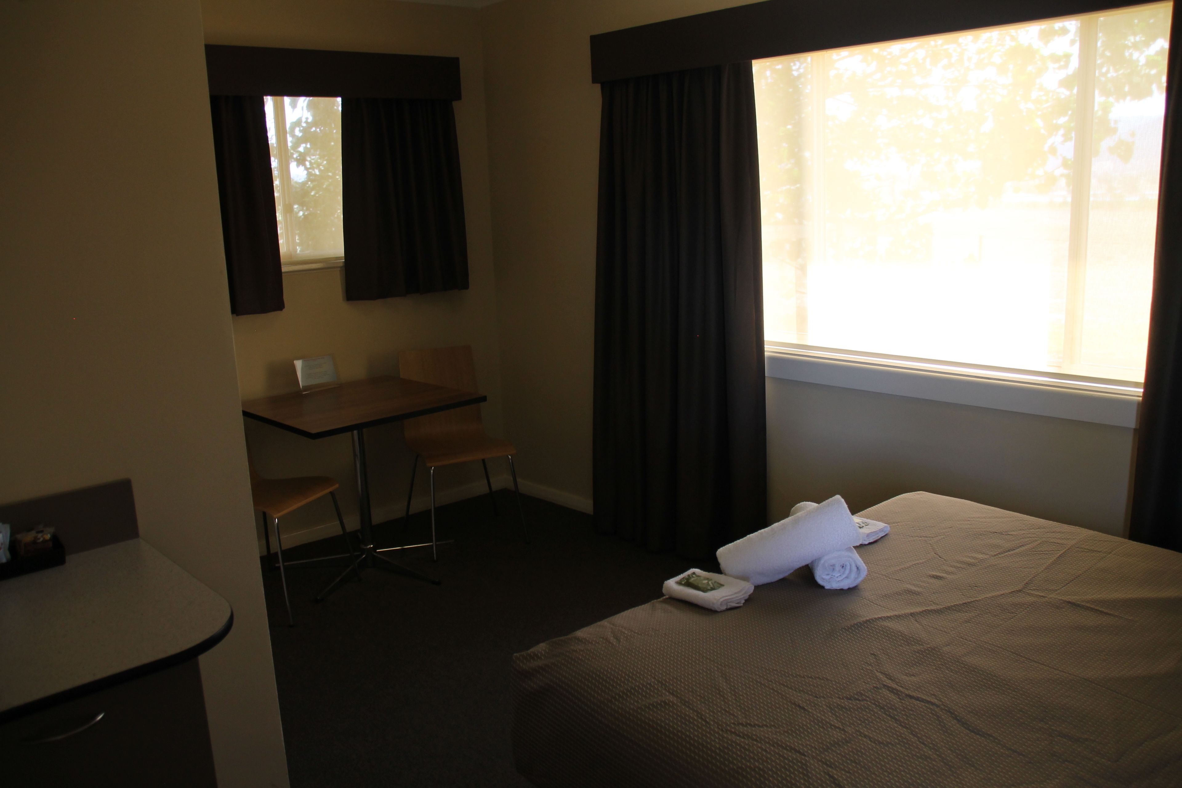 Une chambre d’hôtel avec un lit, un bureau, une chaise et une fenêtre avec des rideaux.