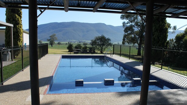 A swimming pool with a view of mountains, surrounded by a fence and covered patio area.