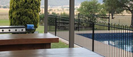 A covered outdoor area with a barbecue grill, a pool, and a view of distant mountains.