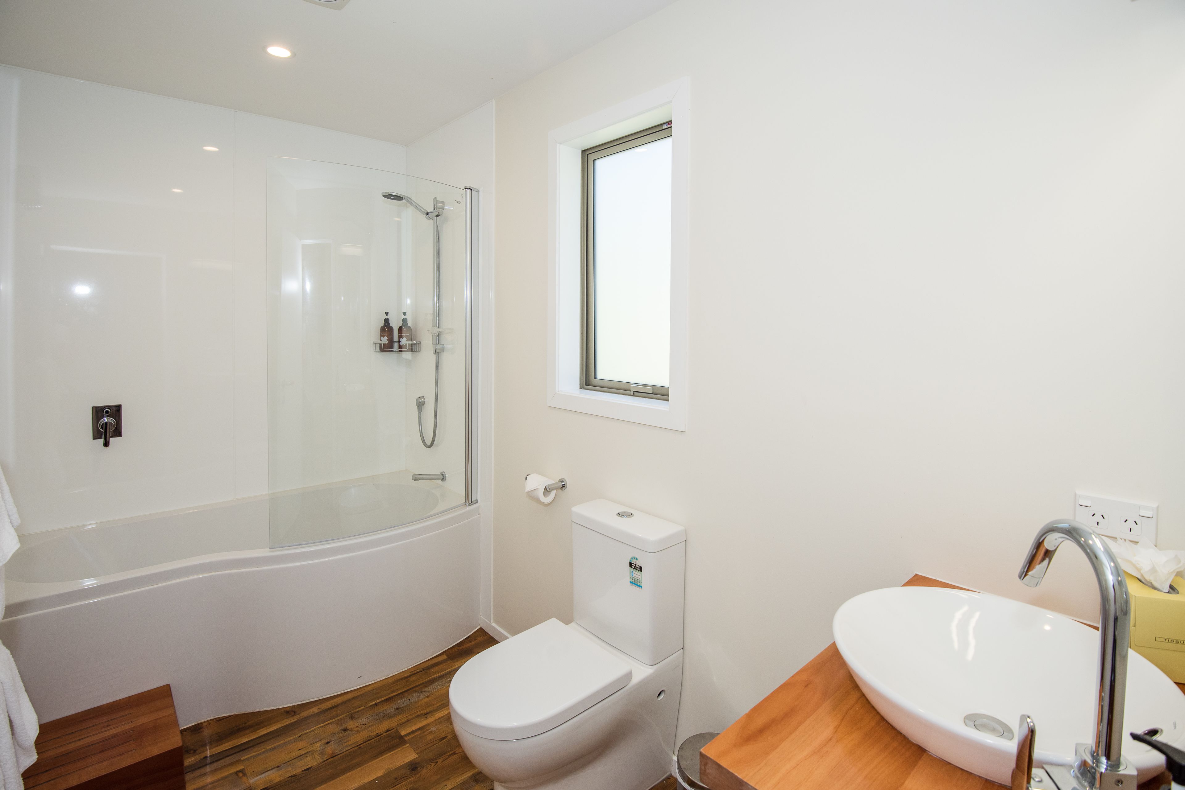 Un baño moderno con ducha envuelta en vidrio, inodoro blanco y tocador de madera con lavamanos.