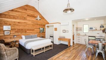 A bedroom with a large bed, a wooden ceiling, a desk, and a kitchenette.
