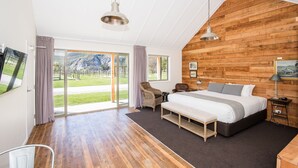 Een ruime slaapkamer met een groot bed, een houten accentmuur, een schuifdeur naar een balkon en een wandgemonteerde televisie.