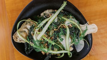 A black skillet containing a dish with meat, mushrooms, and green herbs.