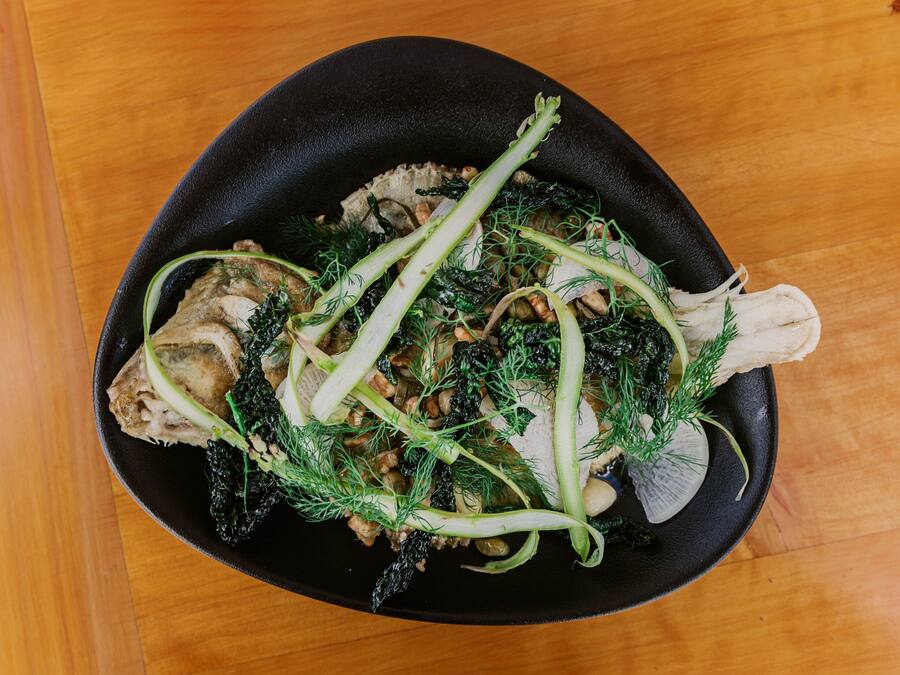 A black skillet containing a dish with meat, mushrooms, and green herbs.