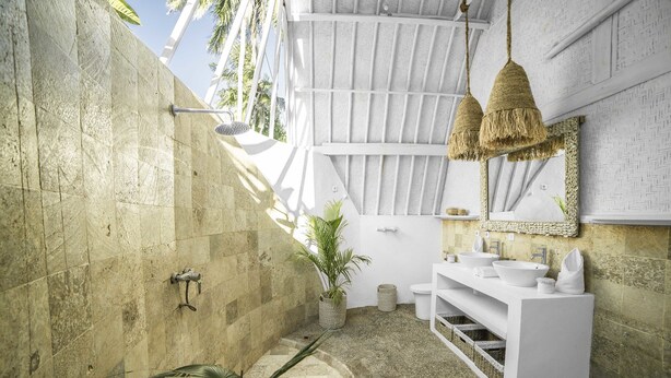 A bathroom with a stone wall, a white sink vanity, a hanging light fixture, and a potted plant. - 7SEAS Cottages (Gili Air)